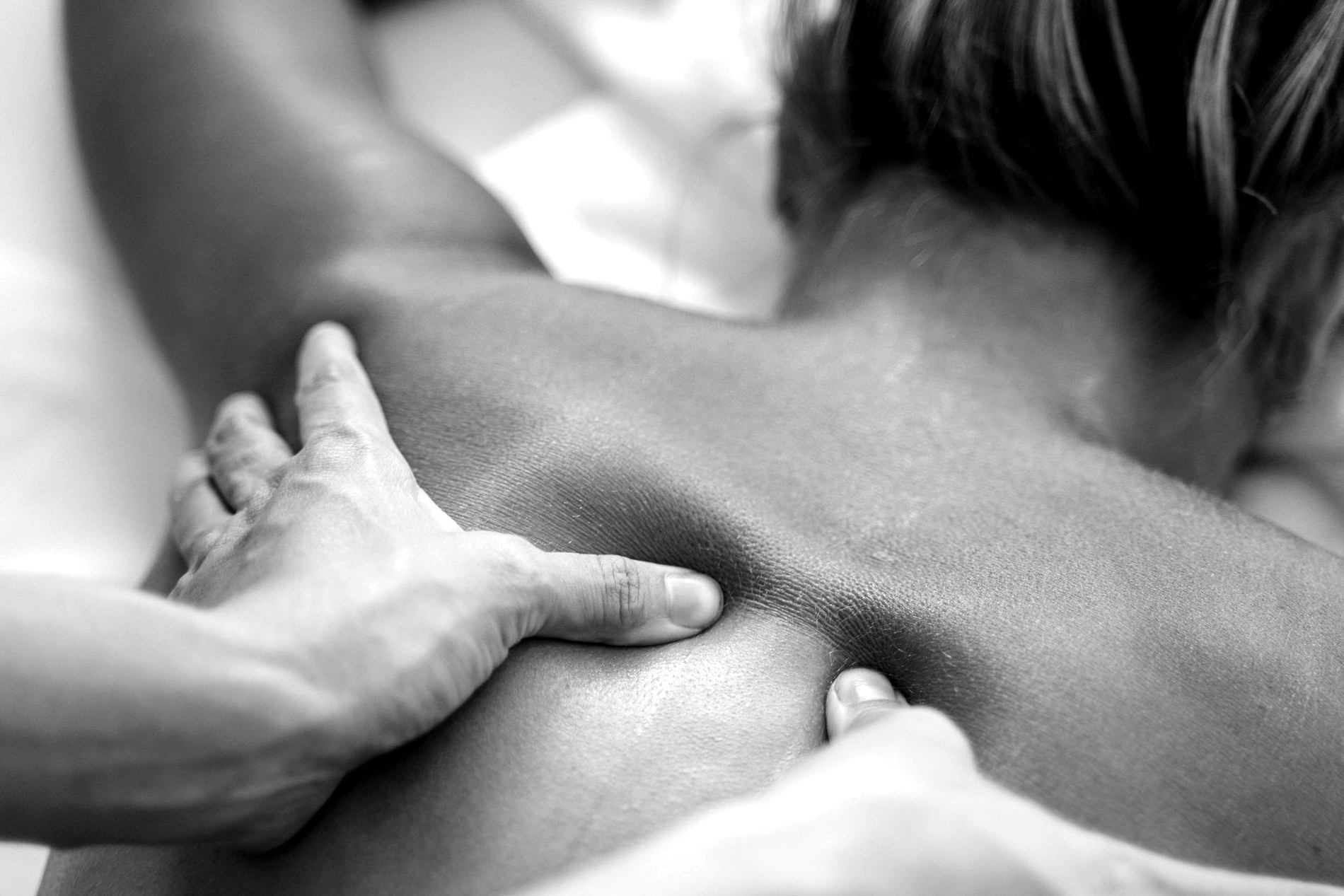 Black-and-white closeup of deep pressure massage work on the upper back.